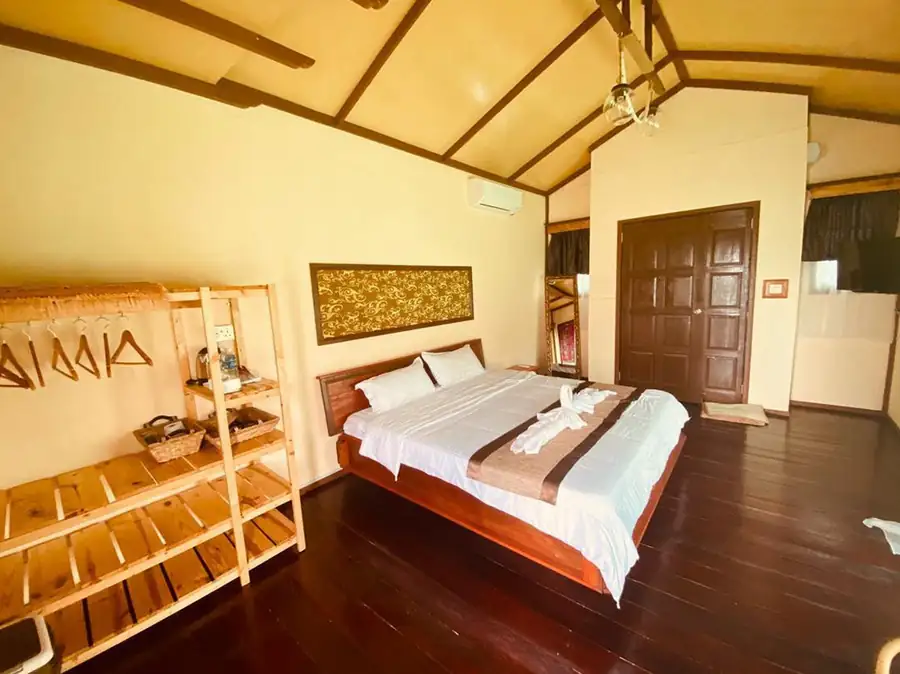 A bright executive room at Parapat Water Village Resort on the Celebes Sea showcasing a large bed facing seamless glass doors, authentic dark wooden floors, and AC.