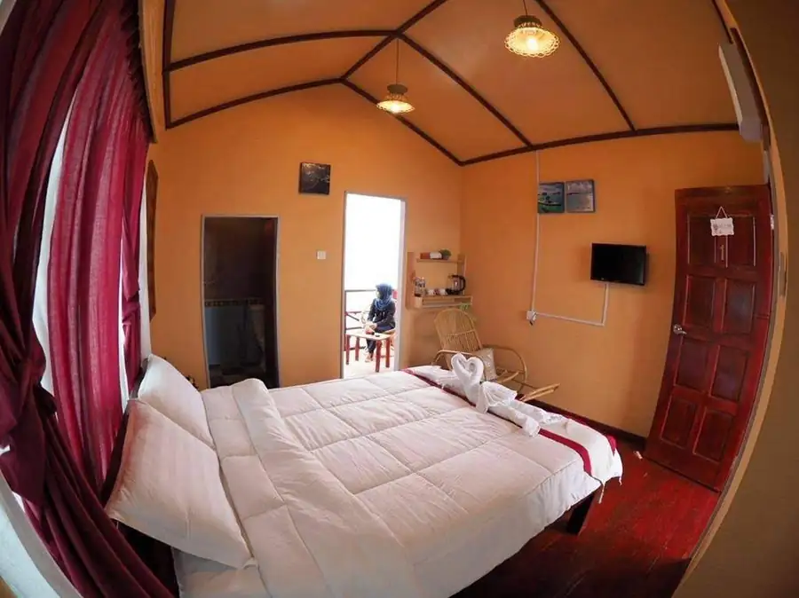 A cozy bedroom at Parapat Water Village Resort near Bum Bum Island featuring a large bed with towel art, rustic timber floor with smooth wooden boards, and air conditioning.